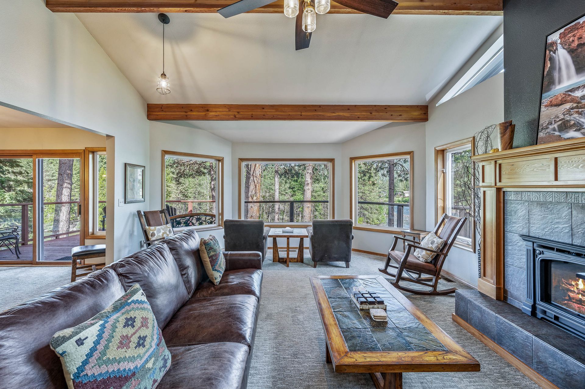 Living room with leather sofa, stone fireplace, large windows overlooking forest.