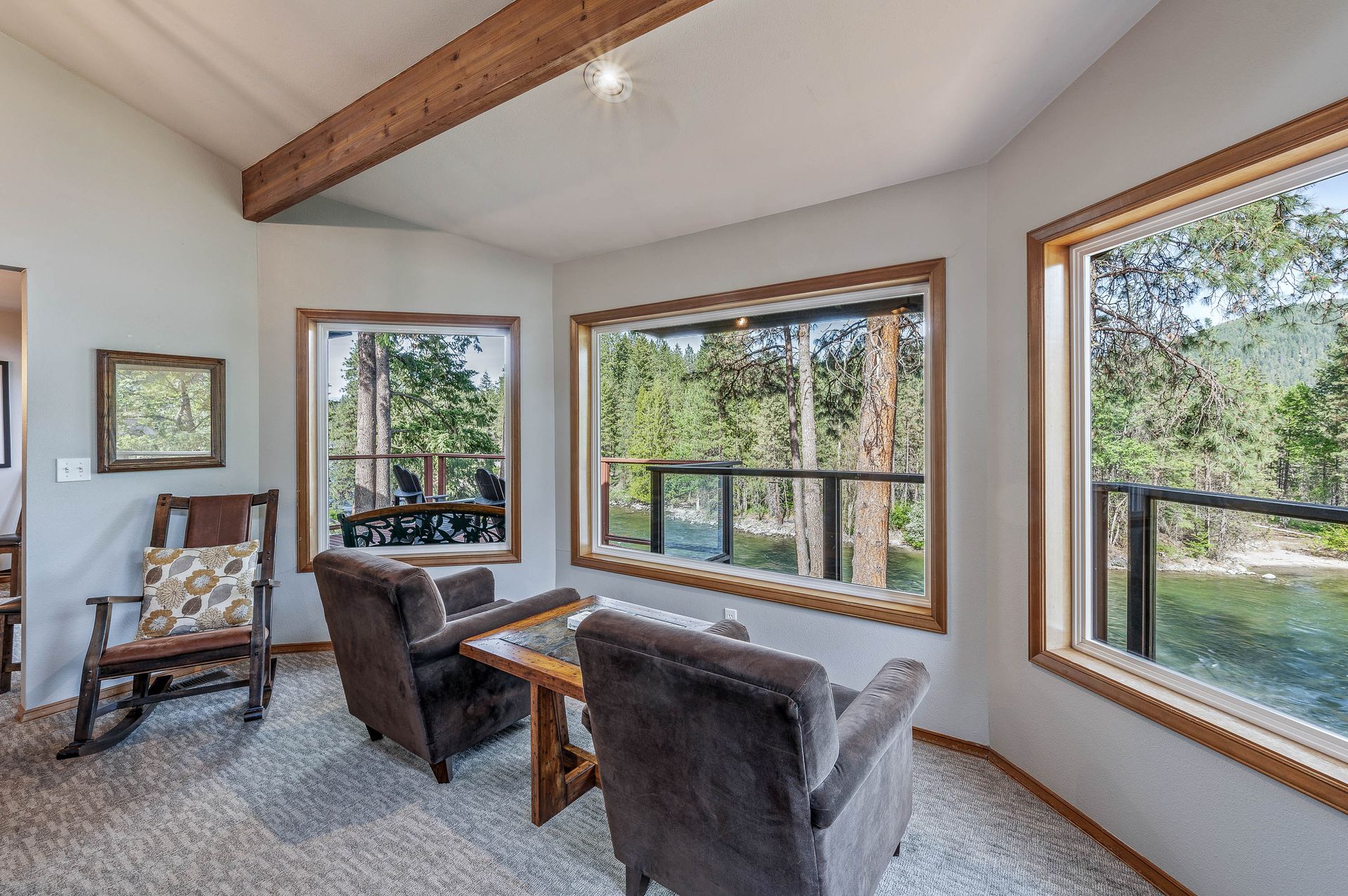Living room with large windows overlooking trees. Two armchairs and a small table.