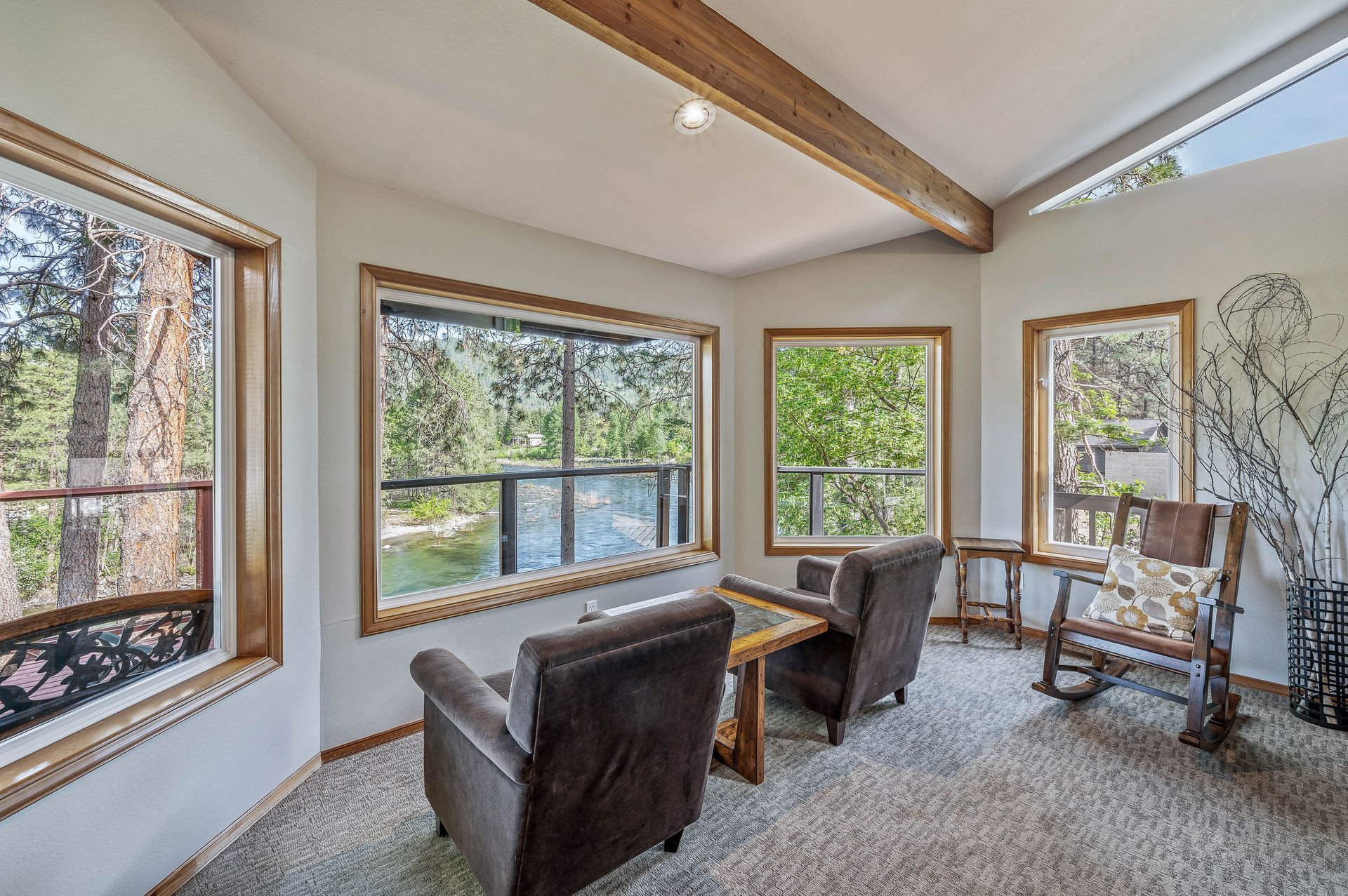 Sunroom with two armchairs, rocking chair, and large windows overlooking a lake.