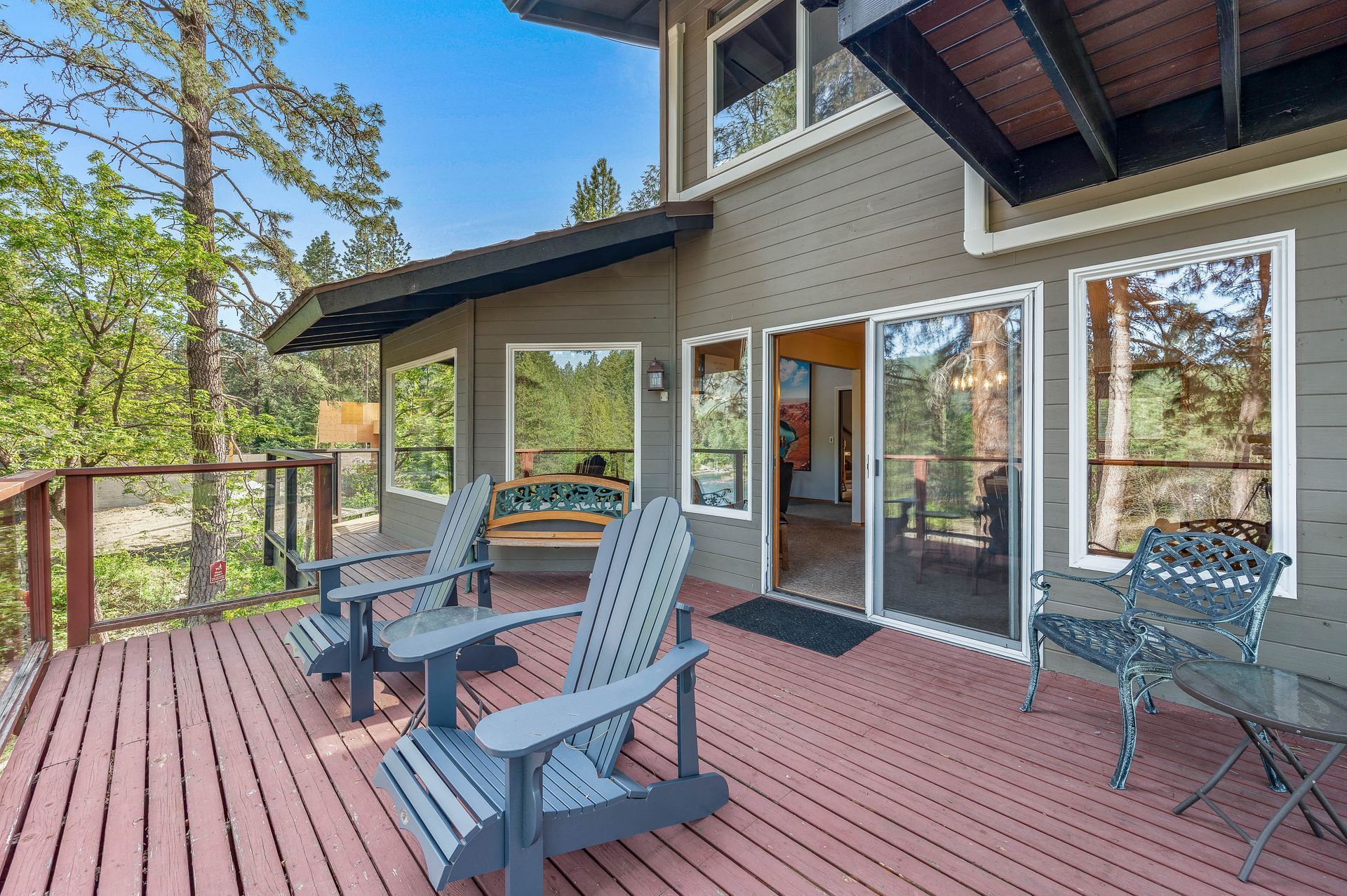 Deck with Adirondack chairs in front of a house with sliding glass doors and a forest backdrop.