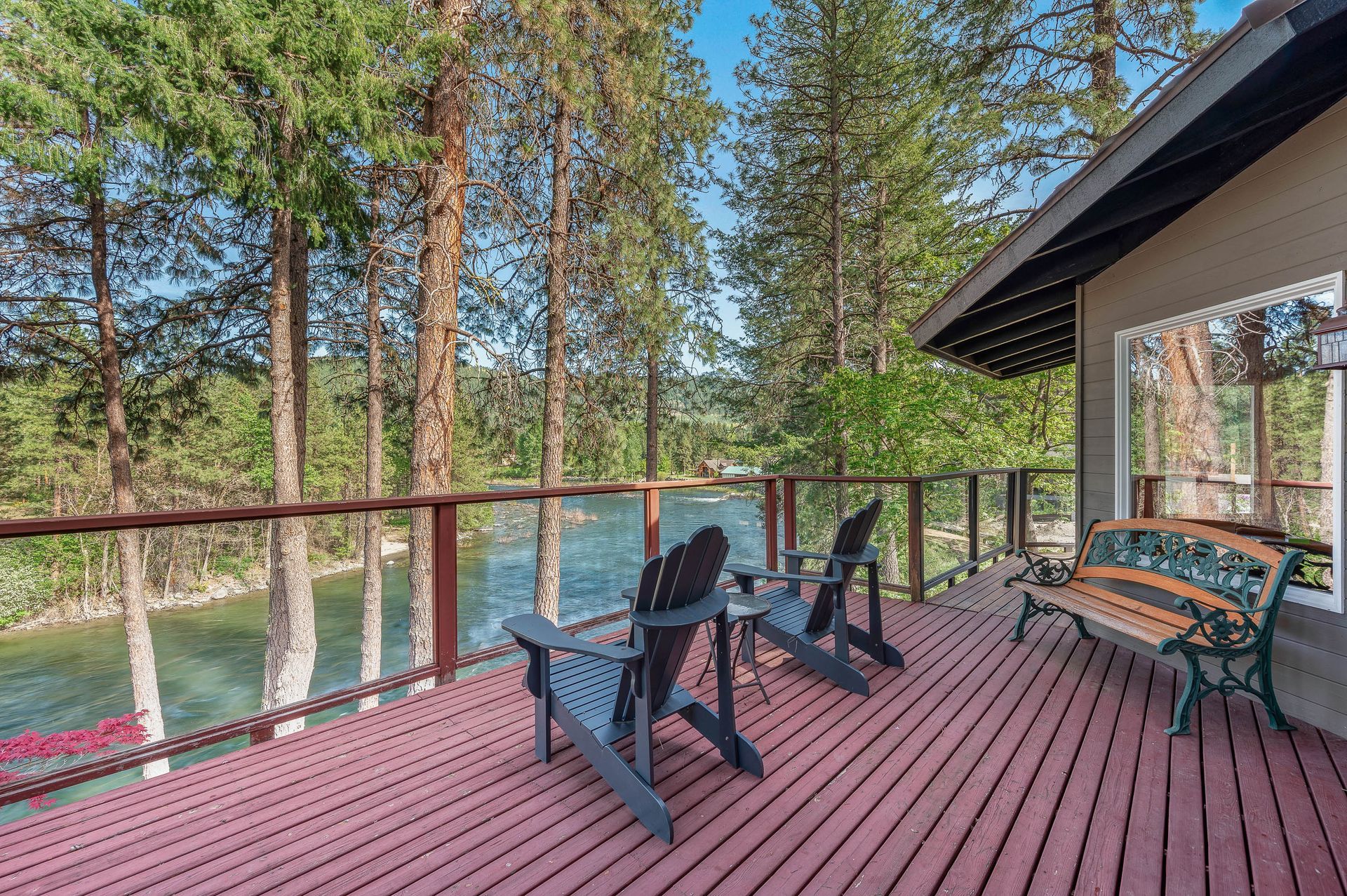 Deck overlooking river with two Adirondack chairs and bench. Trees in the background.