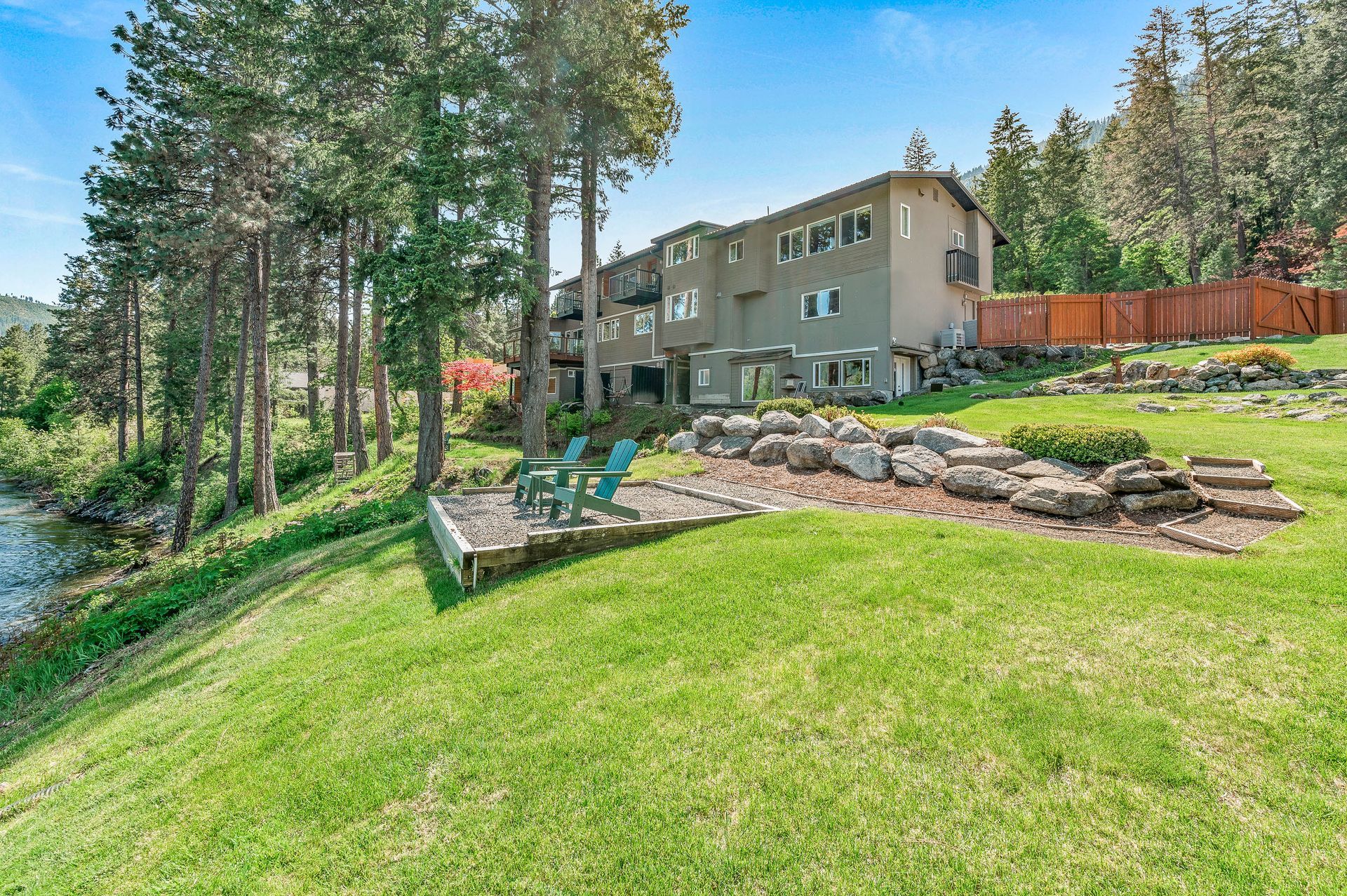 House on a grassy hill overlooking a body of water.  Two blue chairs sit on a patio area.