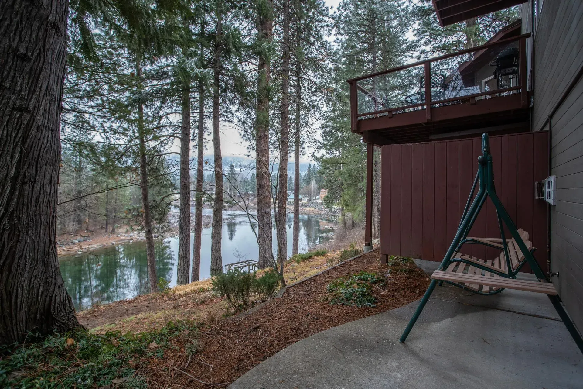 A waterfront home with a deck overlooking a lake, with a swing and trees in the foreground.