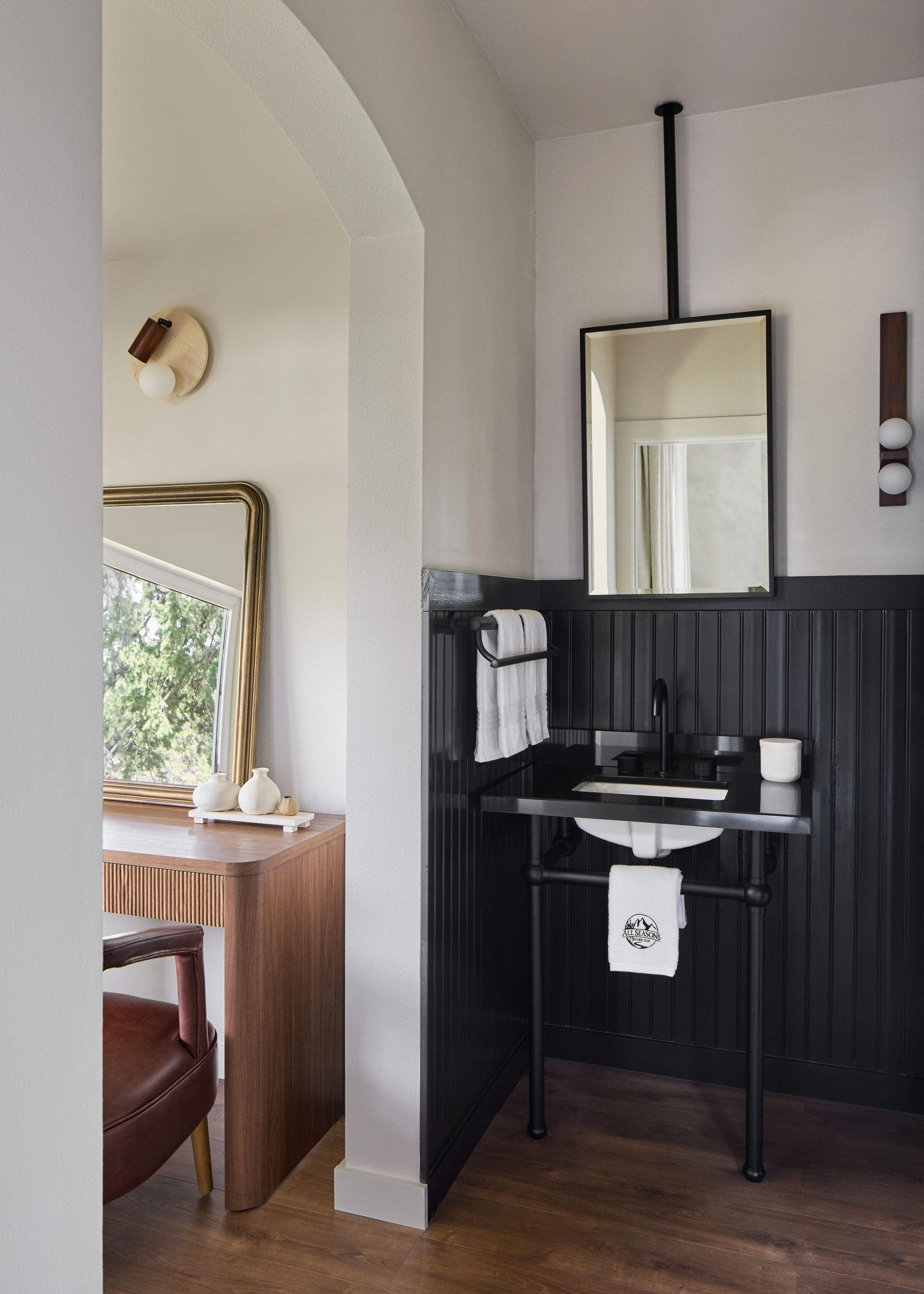 Small bathroom vanity with black wainscoting, mirror, sink, and towel rack beside an arched doorway