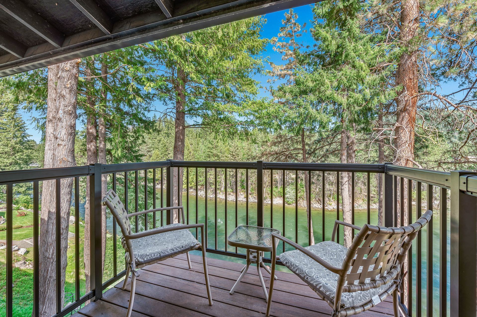 Balcony with two chairs and small table overlooking a body of water and trees.