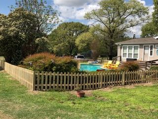 a wooden picket fence surrounds a swimming pool in front of a house .