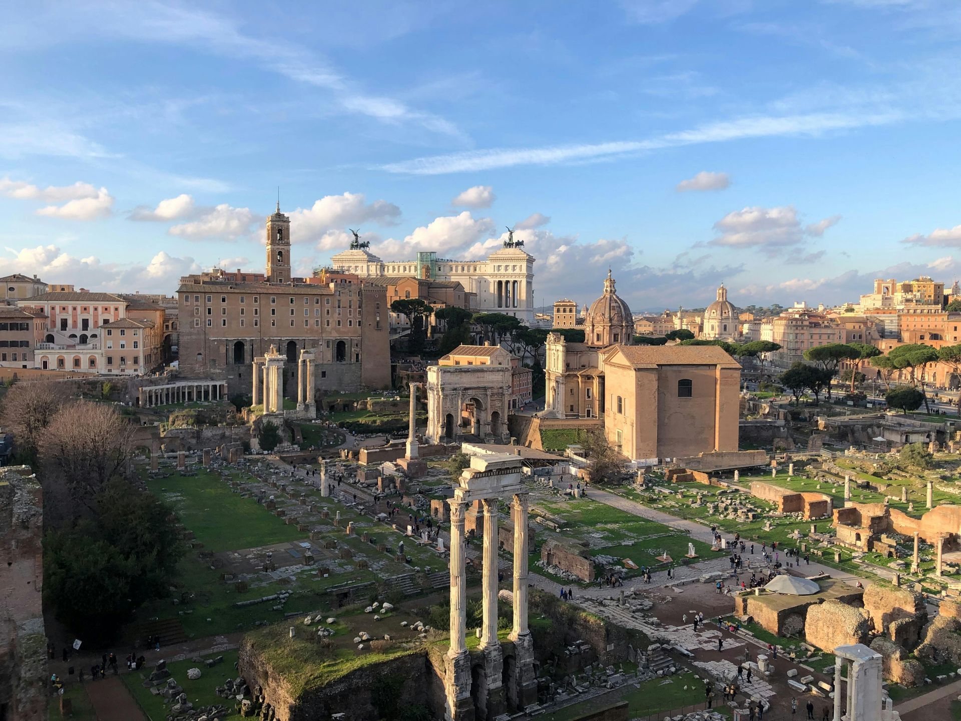 View of the Roman Forum with ancient ruins and historical buildings under a blue sky.