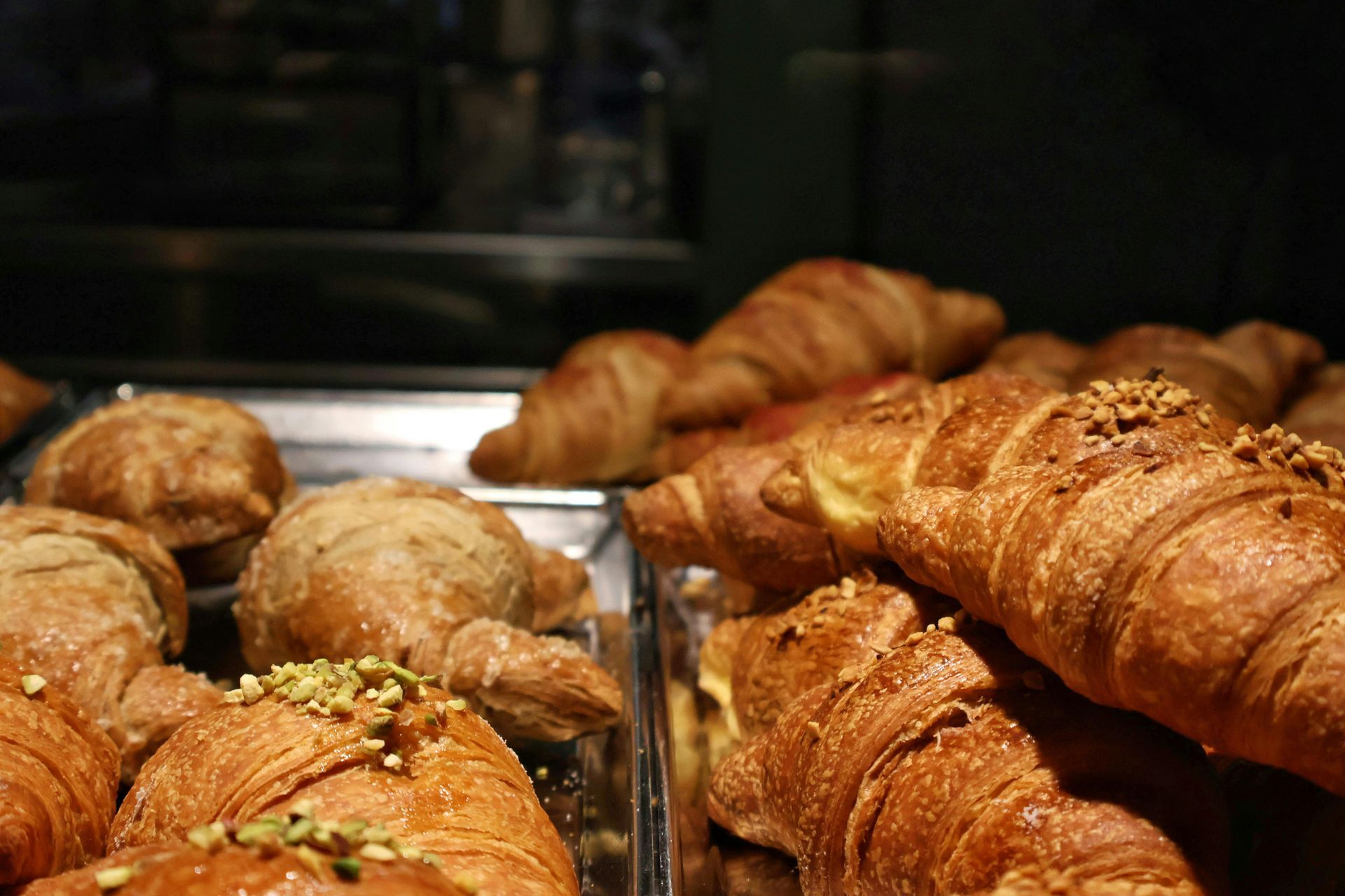 Freshly baked croissants in a bakery display, including pistachio and nut toppings