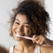 Une femme aux cheveux bouclés se brosse les dents avec une brosse à dents rose.