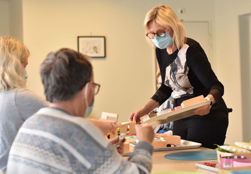 Une femme portant un masque se tient à côté d'un homme assis à une table.