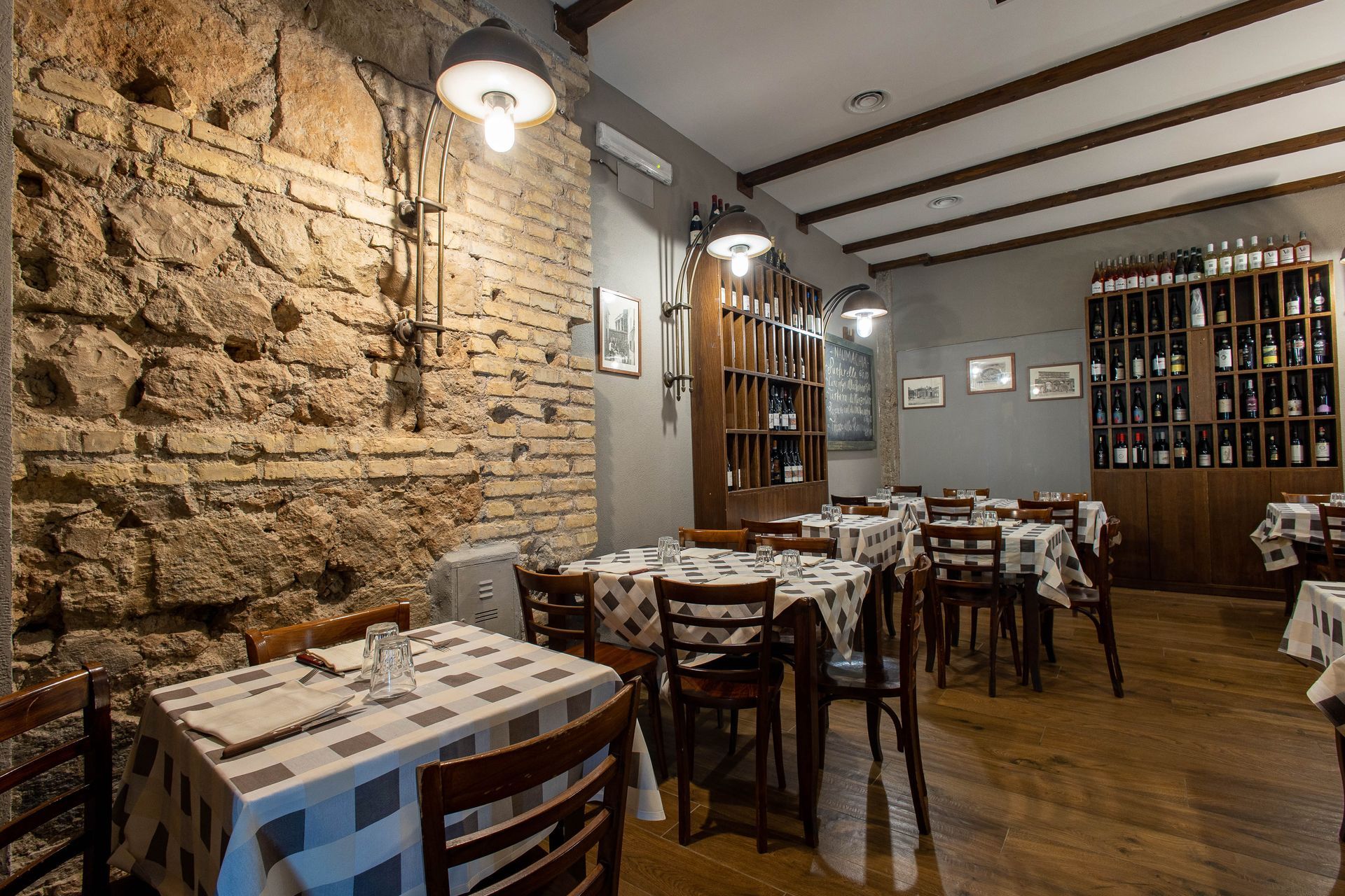 Accogliente interno rustico di un ristorante con pareti in pietra, tavoli in legno e portabottiglie.