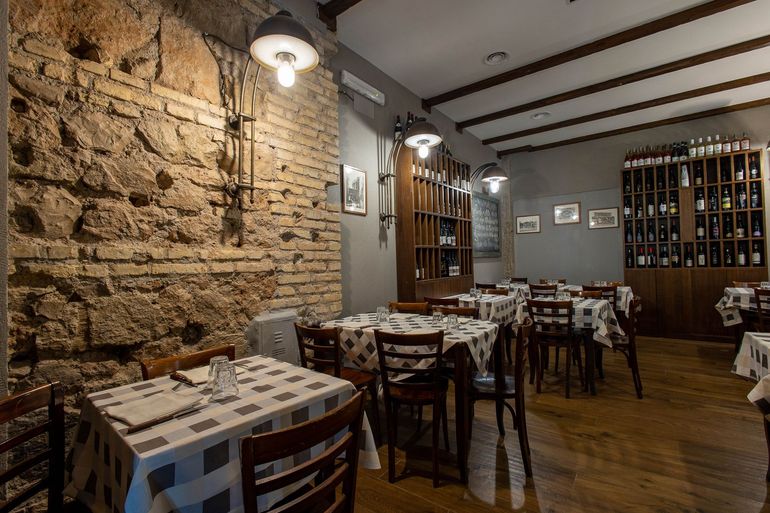 Accogliente sala da pranzo in stile rustico con parete in pietra, tavoli in legno e portabottiglie sulla parete di fondo.