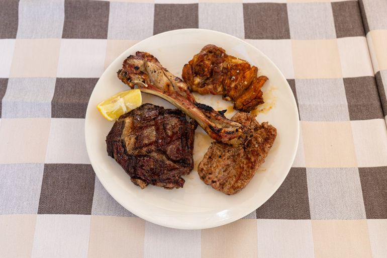 Piatto di carne e pollo grigliati con uno spicchio di limone su una tovaglia a quadri.