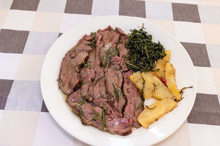 Piatto di carne arrosto affettata con patate e verdure su una tovaglia a quadri.