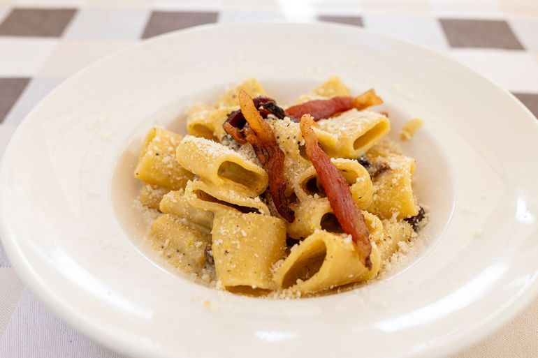 Piatto di rigatoni con pancetta e formaggio grattugiato su un piatto bianco.