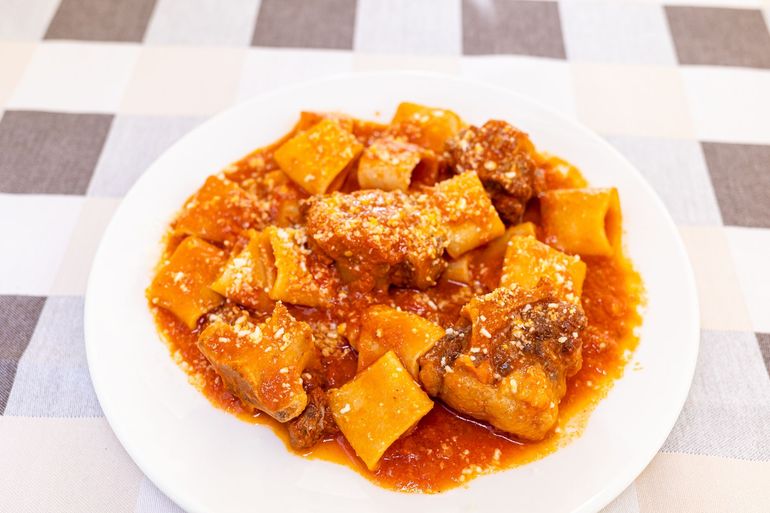 Piatto bianco di ravioli o gnocchi rosso-arancio in salsa, ricoperti di formaggio grattugiato, su una tovaglia a quadri.