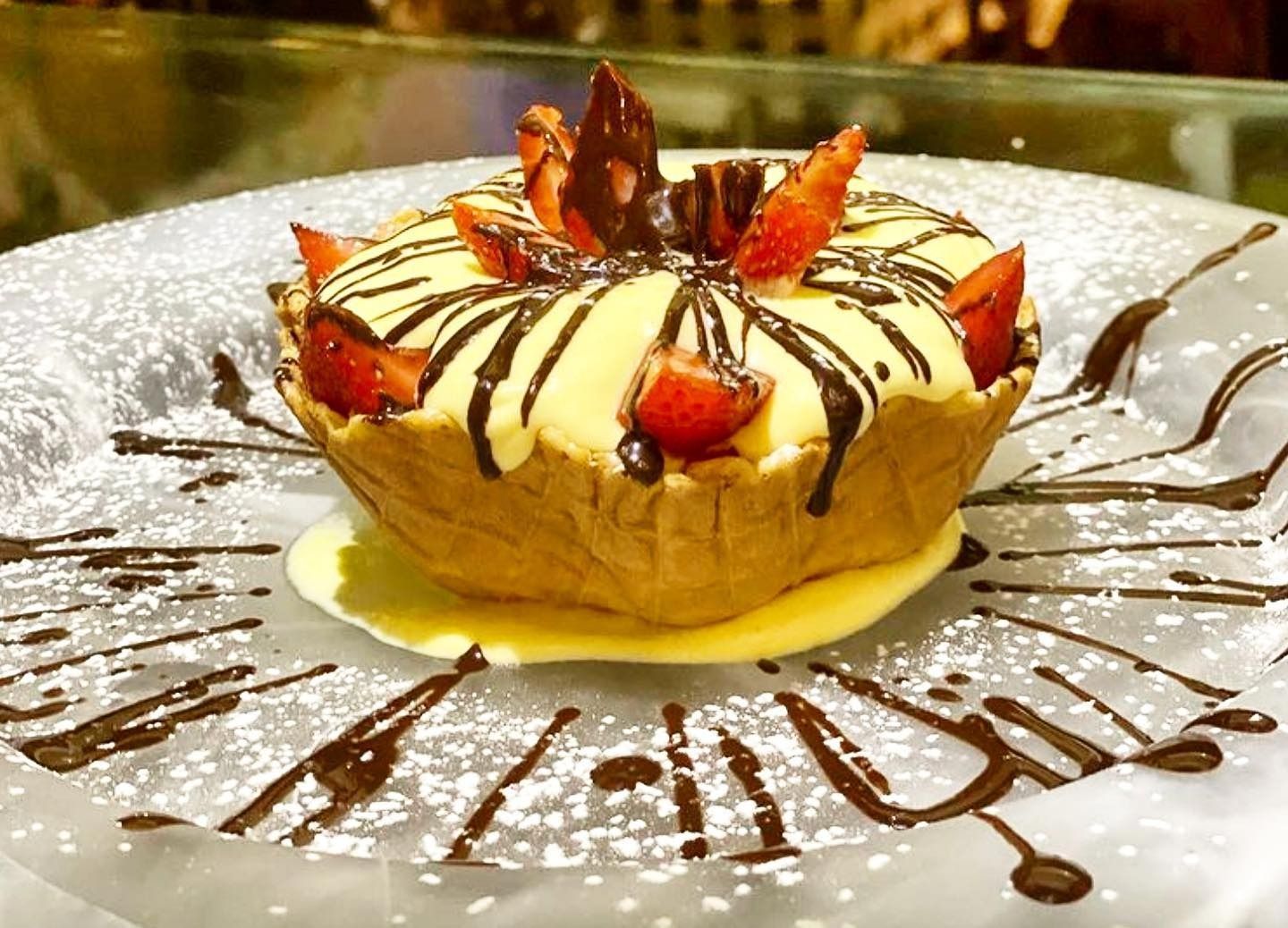Torta dolce con fragole, panna, glassa al cioccolato e salsa al caramello su un piatto bianco.