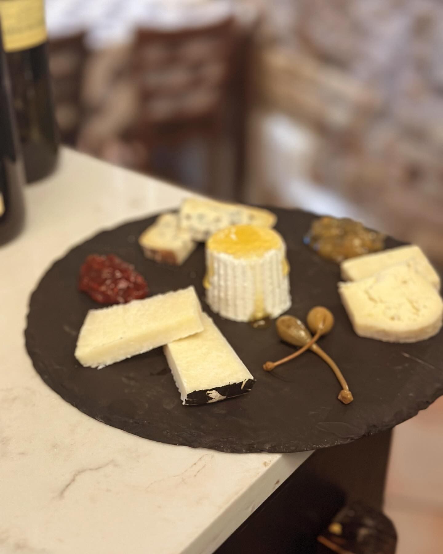 Piatto di formaggi su un tagliere di ardesia con formaggi assortiti, marmellata e cucchiaini di miele su un tavolo