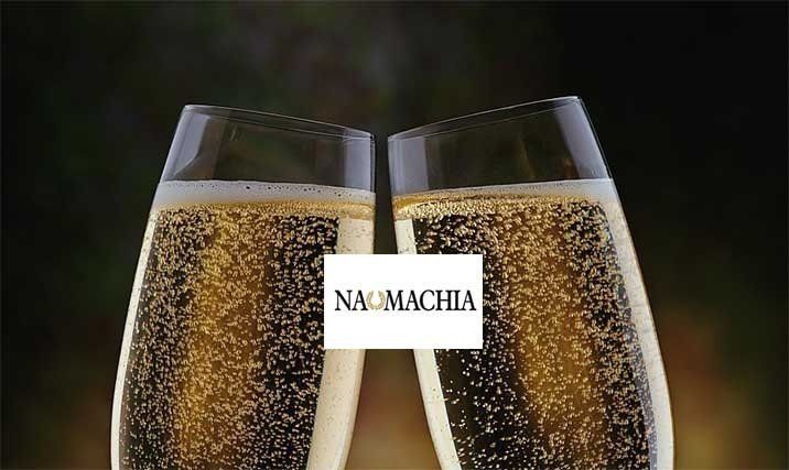 Due flûte da champagne che tintinnano, piene di spumante, con l'etichetta del Noma Chaia al centro.