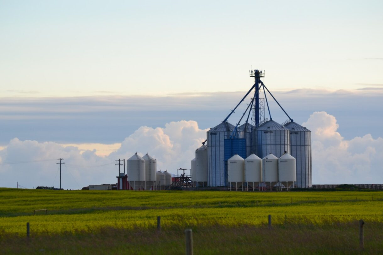 Grain silos on a green field under a cloudy sky.