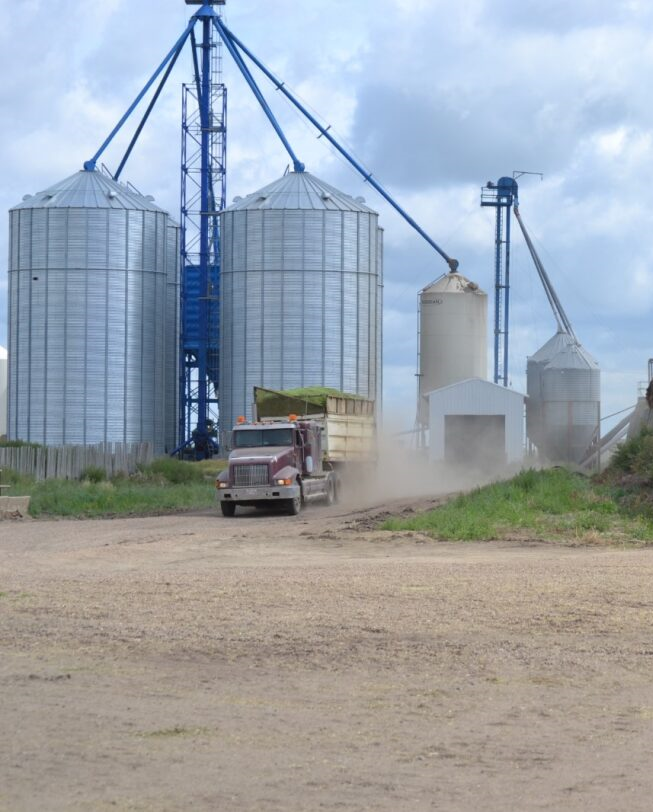 Truck approaching grain silos, kicking up dust on a cloudy day at Coro View Farms Ltd.