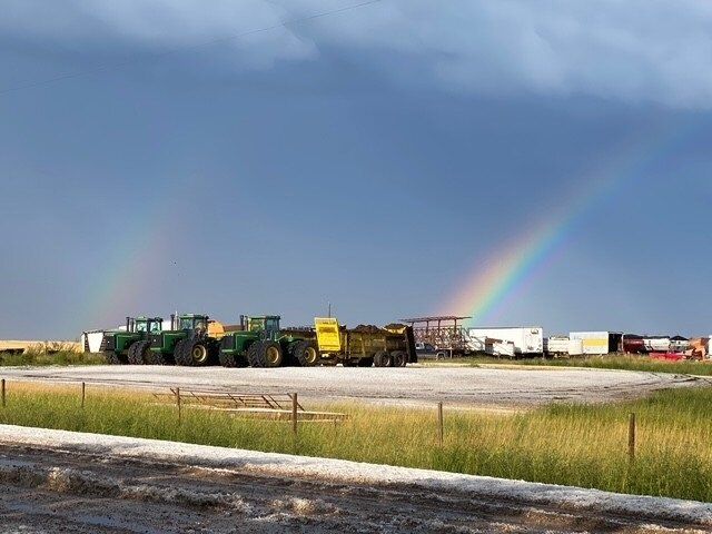 Rainbow over farmyard with green tractors and trailers.