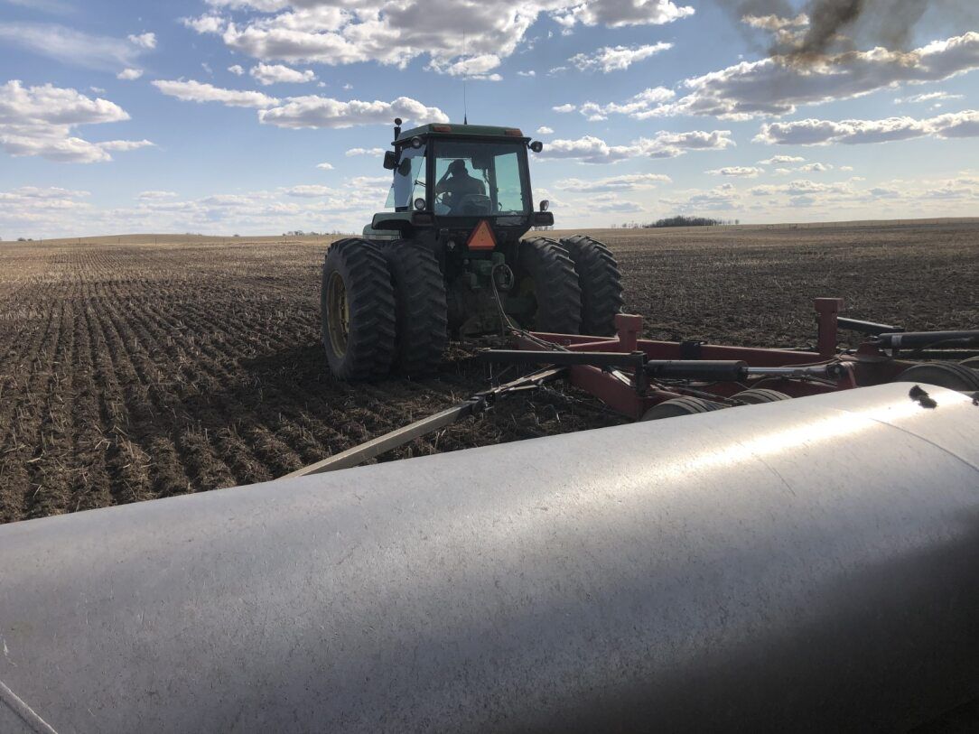 Tractor pulling agricultural equipment across a field under a cloudy sky.