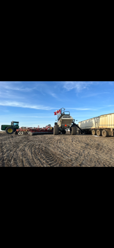 Agricultural scene with machinery harvesting crops in a field under a blue sky.