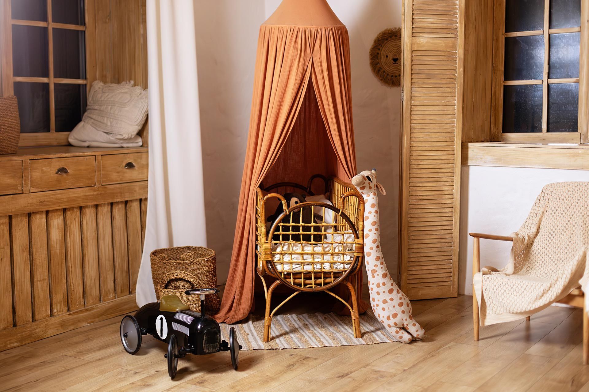 Cozy nursery with wooden accents, a rattan crib under an orange canopy, and a toy car. Cozy nursery with wooden accents, a rattan crib under an orange canopy, and a toy car.