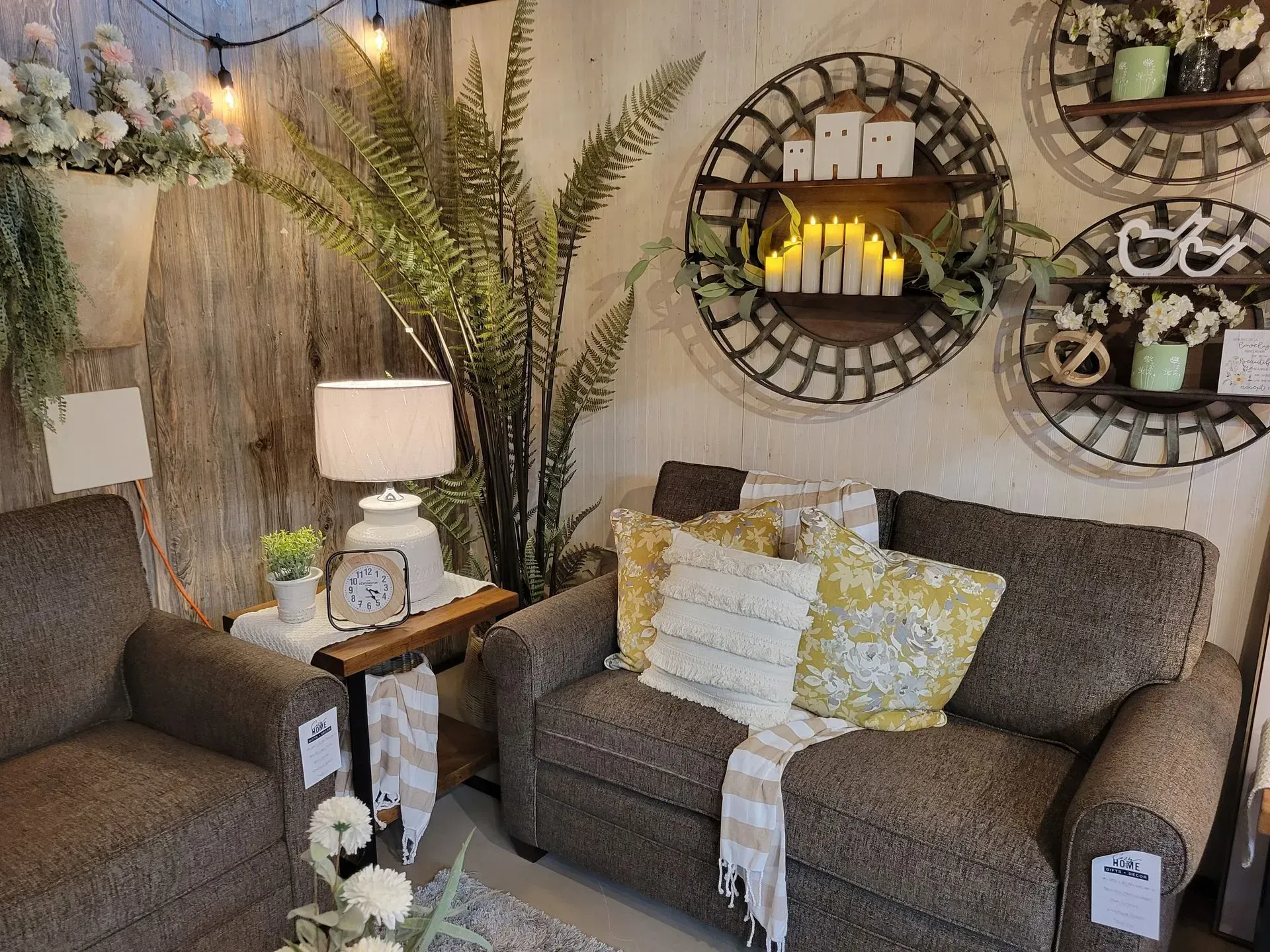 Cozy living room display with brown sofas, decorative pillows, and wall shelves with candles.