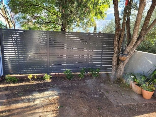 A Slat Fence Surrounds A Backyard Filled With Various Plants And Trees — Anne & Ron Johnson Fencing in Werris Creek, NSW