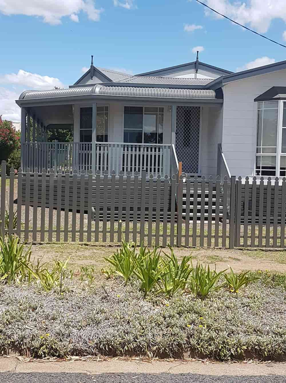 A Small White House With A Wooden Fence In Front Of It — Anne & Ron Johnson Fencing in Werris Creek, NSW