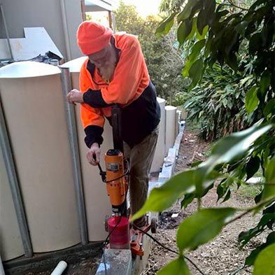 A Man is Using a Machine to Drill a Hole in a Wall — Anne & Ron Johnson Fencing in Werris Creek, NSW