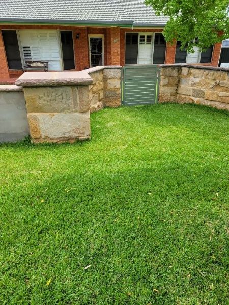 A Brick Wall Encloses A Grassy Yard In Front Of A House, Complete With A Gate For Access — Anne & Ron Johnson Fencing in Werris Creek, NSW