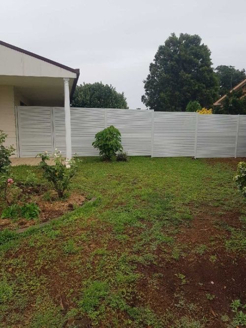 A White Slat Fence Surrounds A Yard With A Vibrant Garden — Anne & Ron Johnson Fencing in Werris Creek, NSW