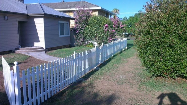 A Classic White Picket Fence Stands Proudly In Front Of A Lovely House, Adding To Its Quaint And Welcoming Charm — Anne & Ron Johnson Fencing in Werris Creek, NSW