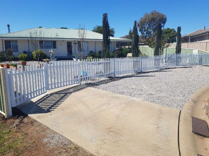 A White Picket Fence With A Gate Surrounds A House — Anne & Ron Johnson Fencing in Werris Creek, NSW