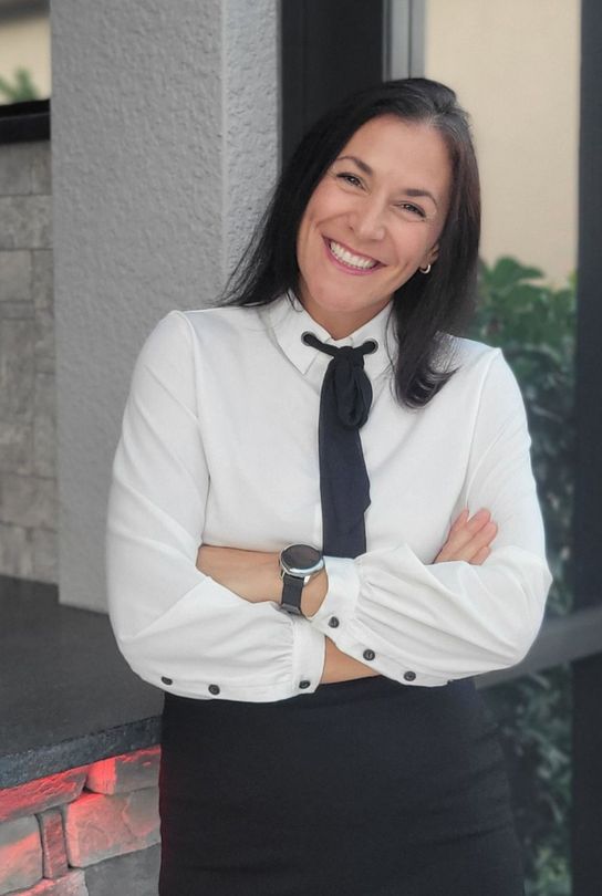 A woman is sitting at a desk with a laptop and a vase of flowers.