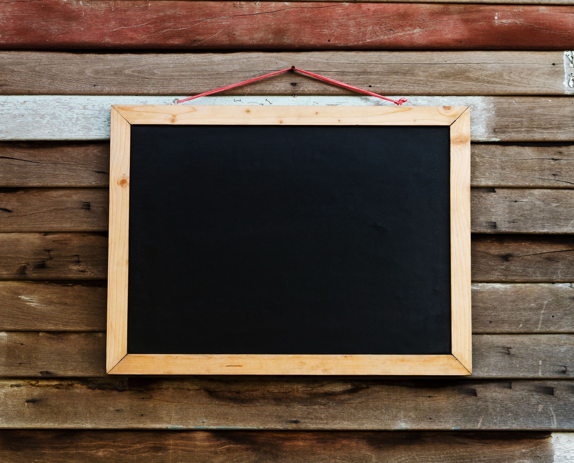 Blank chalkboard sign hanging on a weathered wooden wall