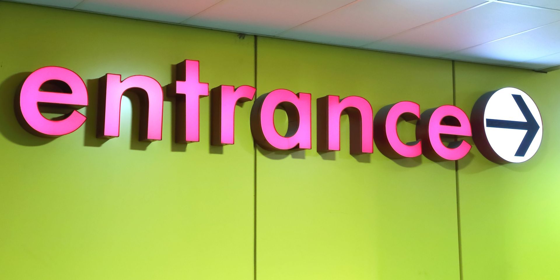 Pink “entrance” sign on a lime green wall with a right-pointing arrow