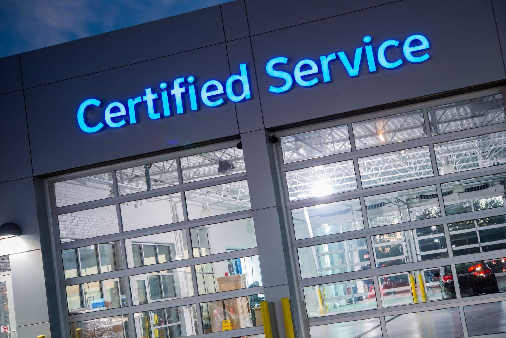 Certified Service storefront with blue neon sign above glass garage doors at dusk