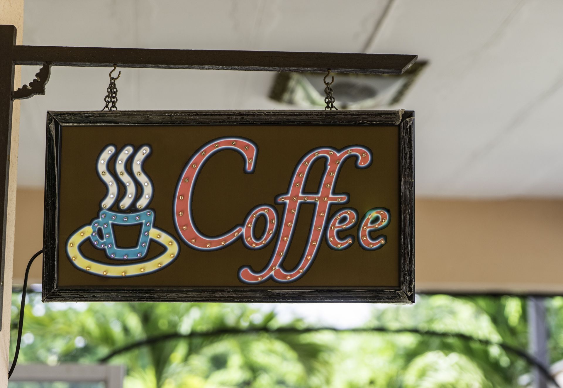 Hanging coffee shop sign with steaming cup illustration and the word “Coffee” in pink script