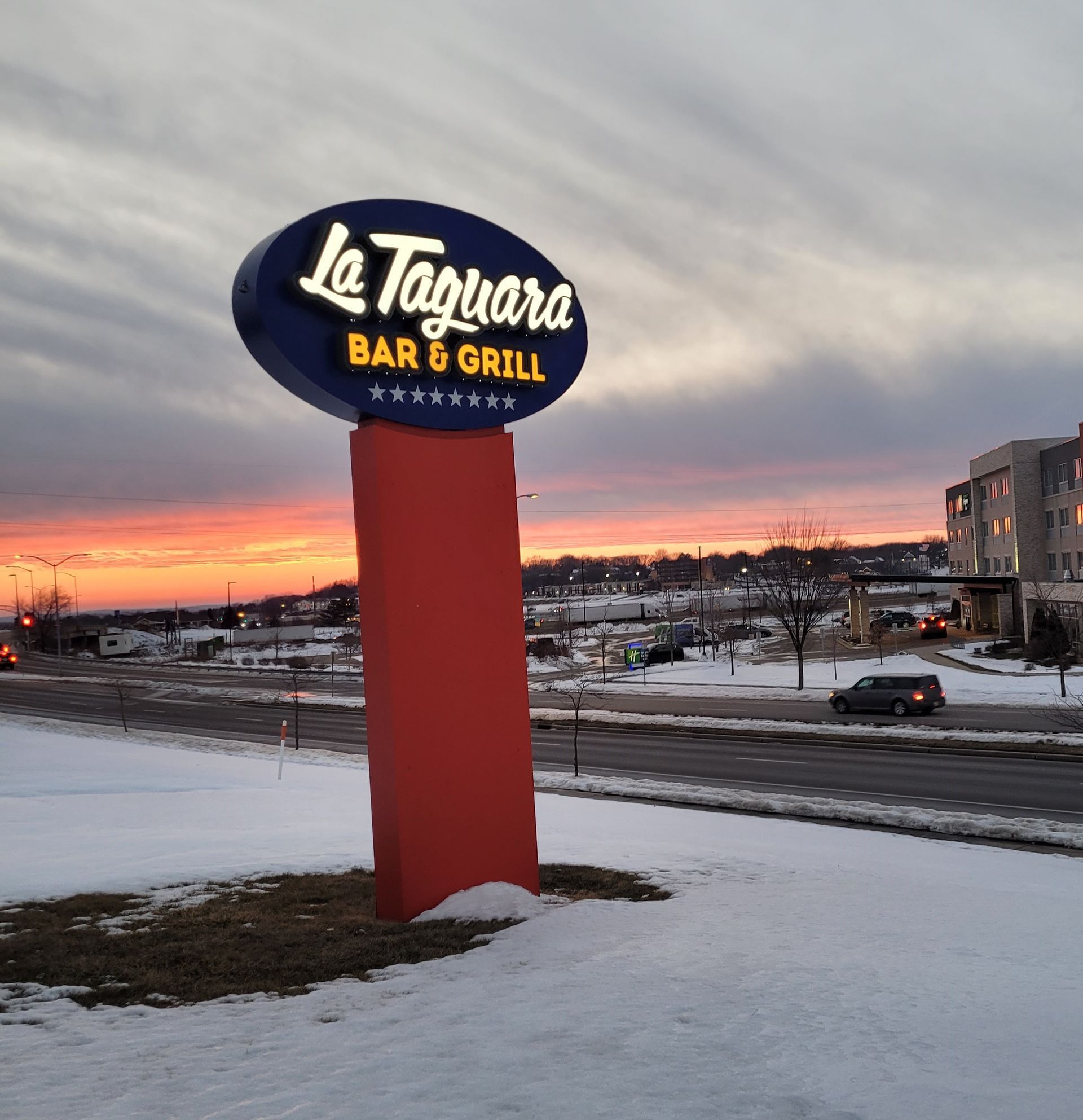 Le Tiguire Bar & Grill sign at dusk beside a snowy roadside under a pink sunset sky