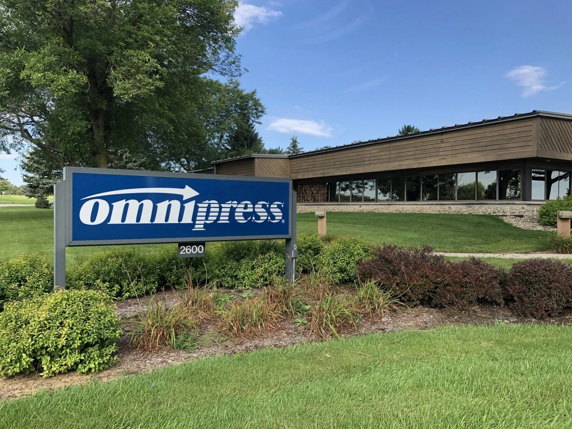 Omnipress sign in front of a low office building, with trees, grass, and a blue sky