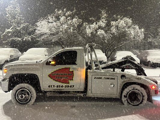 A tow truck is parked in the snow in a parking lot.