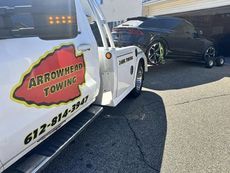 An arrowhead towing truck is parked in front of a garage.