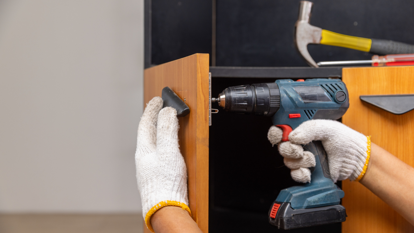 Hands using a cordless drill on a wooden cabinet shelf installation