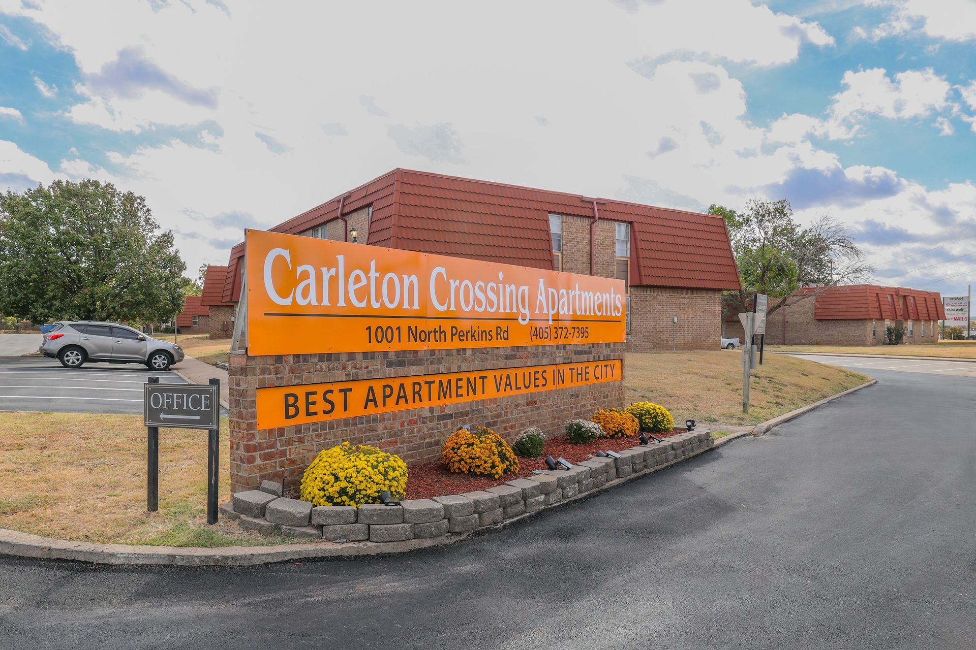 Sign for Carleton Crossing Apartments, orange and white text, flower bed in front.