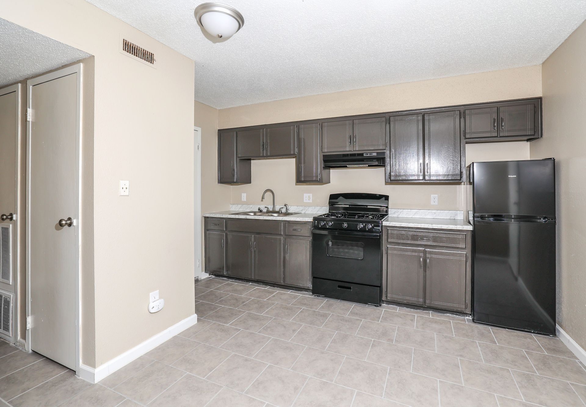Kitchen with dark grey cabinets, black appliances, and light tile floor.