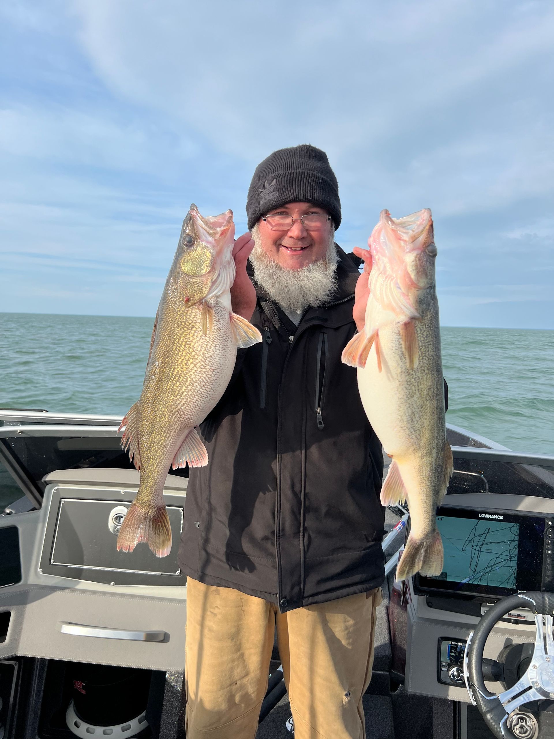 A man with a beard is holding two large fish on a boat.